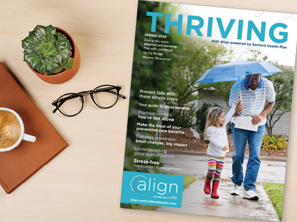 The cover of the Spring 2026 issue of the Thriving Newsletter alongside coffee, eyeglasses, and a potted plant on a table