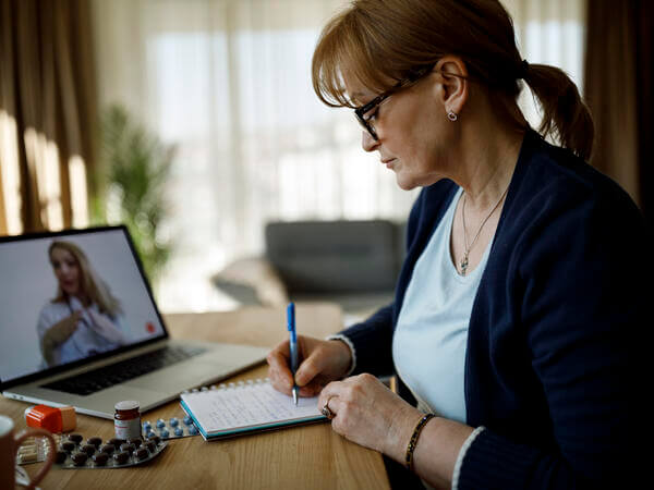 A woman on a video visit on her computer and taking notes