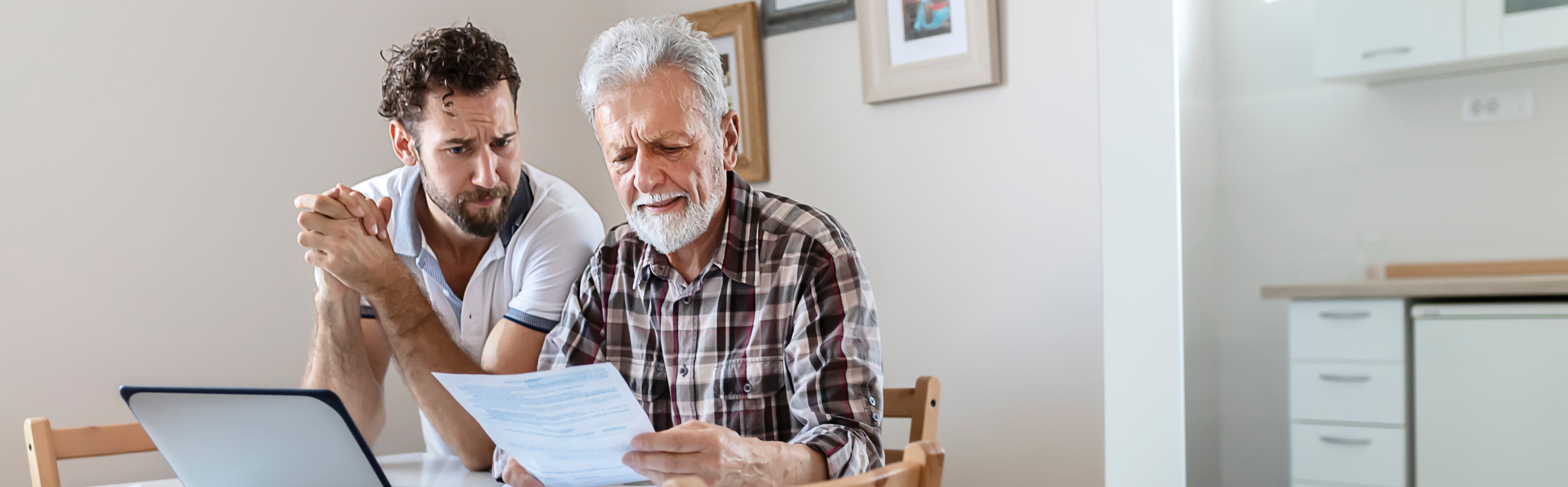 Older man viewing paper with middle-aged man looking over his shoulder