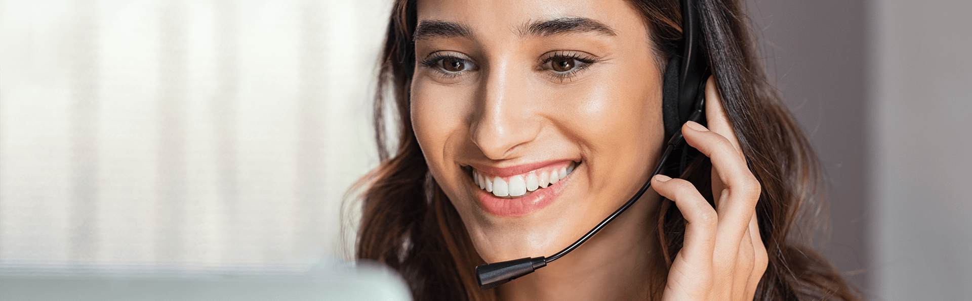 Smiling woman using laptop while talking to customer via her headset.