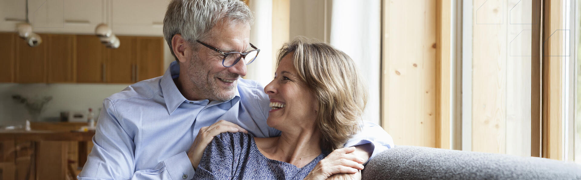 A middle aged couple hugging and smiling on a couch.