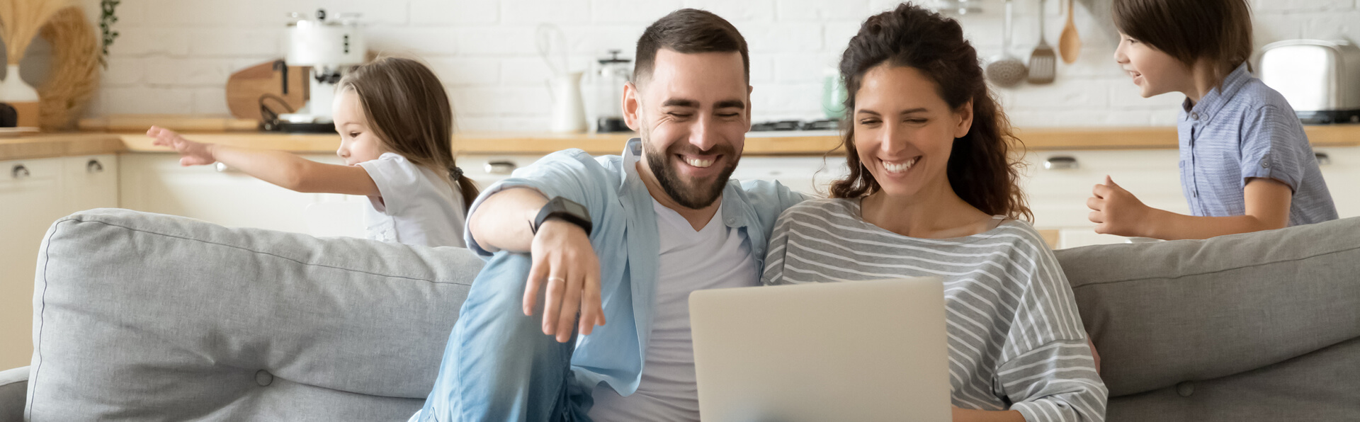 Parents looking at a computer while their children play in the background.