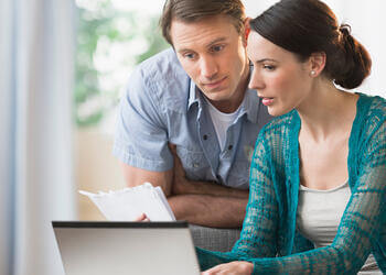 A woman and man looking at papers and their computer comparing notes.
