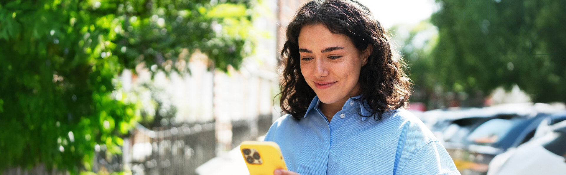 A young woman outside in the sunshine sending a message on her phone.