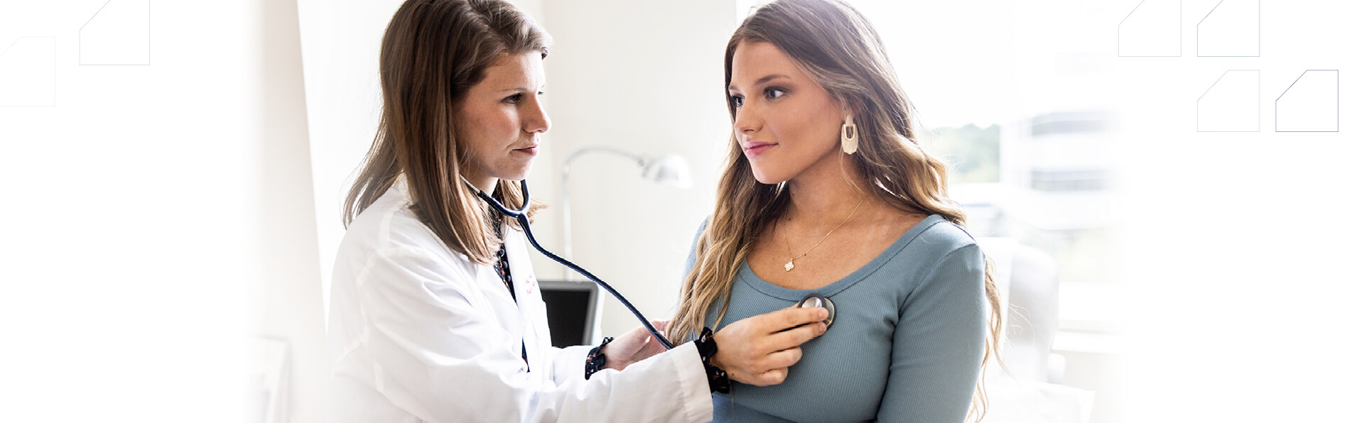 Female doctor listening to female patient's heart with stethoscope in exam room