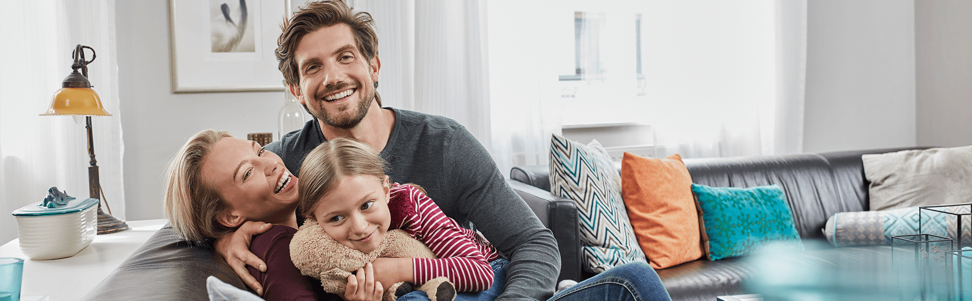 Young Caucasian family of three smiling and laughing on a leather couch.