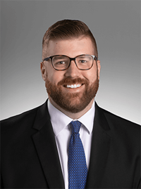 Professional head shot image of Dylan Wheeler in a black suit, white button-up shirt, and blue tie.